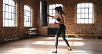 Hispanic young fit woman boxing and kicking a punching bag during her workout training routine at the gym. Powerful young athletic hispanic woman focused on her training routine at the gym