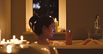 A happy woman texting on her smartphone during a nighttime bubble bath