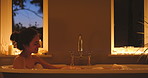 A happy young woman covering herself with bubbles during a candle lit bubble bath