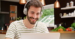 Smiling young man drinking coffee while listening to music and working on his laptop