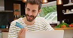 A happy young man making online purchases using his laptop and debit card