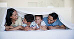 Happy family, kids and parents in bedroom in home, bonding and laughing together at funny joke. Smile, mother and father with children under blanket in bed for love, relax and comfort in the morning