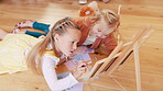 Children, girls and playing with writing in living room of home for child development and creative fun on chalkboard. Family, kids and sisters with talking on floor for games, learning and bonding 