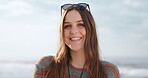 Face, smile and relax with a woman on beach in summer for freedom, vacation or holiday adventure. Portrait, travel and a happy young person or tourist at the sea in nature on blue sky background