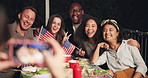 Happy people, friends and photography at night for party, dinner or outdoor event on bench. Group smile in diversity for photograph, picture or memory together by dining table in late evening outside