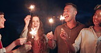 Happy people, sparkles and night in celebration for party, new years or outdoor event together. Group of friends smile and dancing with fireworks in late evening for friendship, memory or fun moment