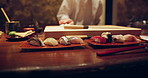 Chef, hands and sushi on plate, table and cleaning with cloth for presentation with fish, food and knife in restaurant. Person, server and cooking for protein, nutrition and meal in diner in Tokyo