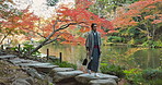 Asian, man is walking in garden in Japan and nature with mindfulness outdoor, lake or pond for peace with culture. Traditional clothes, fresh air and travel, local or tourist in park for zen and calm