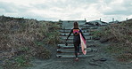 Back, woman and surf at beach, walk up stairs and ready for fitness with wet suit, extreme sport and surfing in nature. Steps, exercise and surfer, ocean with professional or hobby with challenge