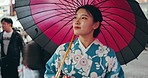 Umbrella, walking and Japanese woman in the city for exploring, journey or adventure on holiday. Street, tradition and young female person in kimono commuting in an outdoor road in urban Tokyo town.