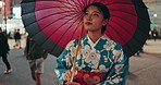 Umbrella, walking and Japanese woman in the city for exploring, journey or adventure on holiday. Street, tradition and young female person in kimono commuting in an outdoor road in urban Tokyo town.