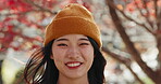 Japanese woman, face and smile in park with a forest, trees and fall with travel and vacation outdoor. Portrait, garden and red leaves with freedom, happy and woods on trip in autumn and calm person