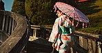 Asian, woman at temple and parasol, walking on bridge with sunshine, tradition and religion with nature. Traditional clothes, culture and wellness, Japanese with travel and umbrella for sun outdoor