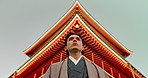 Asian, man at temple in Japan and religion, low angle view for mindfulness, culture and tradition. Worship, peace and walking in traditional clothes outdoor with Japanese architecture and landmark