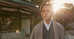 Asian man is walking, temple and garden with sunshine or lens flare, mindfulness and zen in the morning outdoor. Young worshipper in traditional clothes, culture and religion with nature and calm