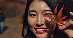 Woman, Asian and face with leaf in autumn, nature and color with happiness outdoor. Environment, plant and smile in portrait, park or garden in Japan with foliage, mockup space and positivity