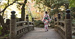 Woman, back and walking in garden with kimono or Japanese fashion on bridge in forest. Traditional, style and girl with dress robe from culture travel in spring nature, woods or park with trees