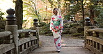 Japanese, fashion and woman in kimono outdoor walking with bag on bridge in garden or forest. Traditional, style and girl with culture dress robe relax in nature, woods or park with peace and zen