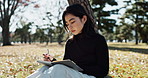 Japanese woman, writing and book in park for thinking and relax for leisure in nature to journal experience. Young person, wellness or personal diary in tokyo city, peace or creative idea in notebook