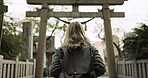 Woman, nature and torii gate in Kyoto with backpack, tourist and back with traditional history. Architecture, japanese culture and shinto shrine in woods with sculpture, memorial and monument