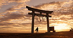 Torii gate, sunset and man at beach with surfboard, spiritual history and travel adventure in Japan. Shinto architecture, Asian culture and calm ocean sky in Japanese nature with sacred monument.