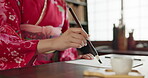 Brush, ink and hand with Asian writing or script on paper, document and creativity with calligraphy and traditional text. Japanese font, writer with black paint and person at desk with art and tools