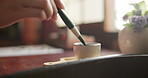 Brush, ink and Japanese calligraphy with hands writing at desk with creative vintage culture with person in home. Paintbrush, traditional script and artist painting text on paper, letter or journal.