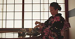 Japanese woman, pot and tea cup for ceremony with health, wellness or liquid to relax at tearoom table. Lady, person and pouring with drink for culture, detox or peace with indigenous clothes in home