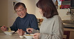 Senior couple, eating noodles and home with chopsticks, conversation and happy at dinner for nutrition. Japanese woman, man and food in retirement with smile, talking and diet for wellness in Tokyo