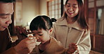 Asian parents, girl and feeding at dinner with smile, help and care with bonding, night or nutrition in family home. Child, mother and father with food, diet or spoon in dining room at house in Tokyo