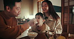 Asian parents, kid and feeding at dinner with smile, help and care with bonding, night or nutrition in family home. Child, mother and father with food, diet and spoon in dining room at house in Tokyo