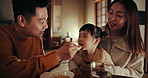 Asian parents, child and feeding at dinner with smile, help and care with bonding, night or nutrition in family home. Kid, mother and father with food, diet and spoon in dining room at house in Tokyo