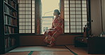 Thinking, morning and traditional Asian woman by window for reflection, calm and wellness. Kimono, culture and happy person in home with view for thoughtful, wondering and relaxing in living room