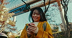 Japanese woman, phone and texting in park, happy and excited with reading notification by monorail. Girl, person and smile with smartphone with click, thinking and backpack with social media in Tokyo