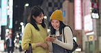Japanese women, phone and city for night travel with social media, happy news or information. People or friends talk and laugh with mobile for network, funny meme or communication in Tokyo and bokeh