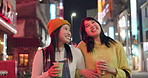 Japanese, friends and walking with a drink in the city at night with happy conversation of travel. Tea, takeaway or women smile together talking on coffee break with bonding, experience or funny chat
