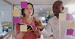 Business people, writing and teamwork on glass board for project workflow, brainstorming and goals with digital tablet. Man and woman or editor with ideas, creative sticky notes or strategy in office