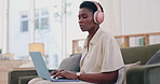 African woman, laptop and headphones on sofa for remote work from home with typing for social media management. Person, freelance worker and computer with music, content creation or web blog on couch