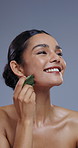 Face, gua sha and beauty with woman massage skin for facial, treatment and smile on grey background. Jade, cosmetics tools and skincare, happy model with dermatology in studio, self care and wellness