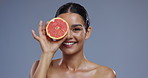 Skincare, grapefruit and face of woman on blue background for wellness, beauty and cosmetics. Dermatology, spa facial and person with fruit for nutrition, organic and natural benefits in studio
