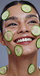 Woman, face and happy with cucumber in studio for organic treatment, anti aging or natural cosmetics. Model, vegetable and smile with dermatology for detox, healthy skin and beauty on gray background