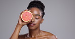 Grapefruit, beauty and woman in studio for healthy glow, vitamin c benefits or collagen on grey background. African model, citrus fruits and dermatology for skincare, eco cosmetics or detox nutrition