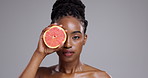 Beauty, face and woman with grapefruit in studio for vitamin c benefits, detox and glow on grey background. Portrait, serious african model and citrus fruits for skincare, sustainability or nutrition