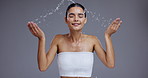 Water splash, skincare and face of woman on gray background for cleaning, wellness and cosmetics. Dermatology, beauty and person with drops for washing, facial treatment and healthy skin in studio