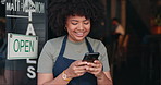 Happy black woman, phone and open cafe by door for communication, social media or networking. African female person or waitress smile on mobile smartphone in online chatting or texting at coffee shop