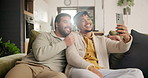 Happy, gay couple and selfie in living room, home and embrace in couch, love and lgbtq. Young, smile and house for commitment, bonding together and romantic relationship for social media post
