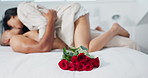 Couple, red roses and lying on bed for anniversary, love or valentines day in romance, embrace or trust at home. Romantic man and woman in bedroom intimacy, passion or bonding with flowers at house