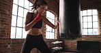 Slow motion young athletic woman hitting a punching bag during her workout routine in the gym. Fit, focused hispanic woman kicking and boxing a punching bag during her cardio training routine.