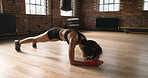 Focused young woman on the floor doing planks timing her progress on her cellphone.Athletic hispanic woman working on her core with bodybuilding plank exercises during her workout routine in the gym.