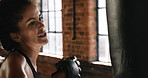 Serious sporty woman hitting a punching bag during her cardio workout. Fit woman in the gym during her cardio boxing routine using a punching bag.Young woman kicking and hitting a punching bag